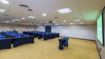 A conference room with rows of tables and chairs, a projector screen, and a carpeted floor.