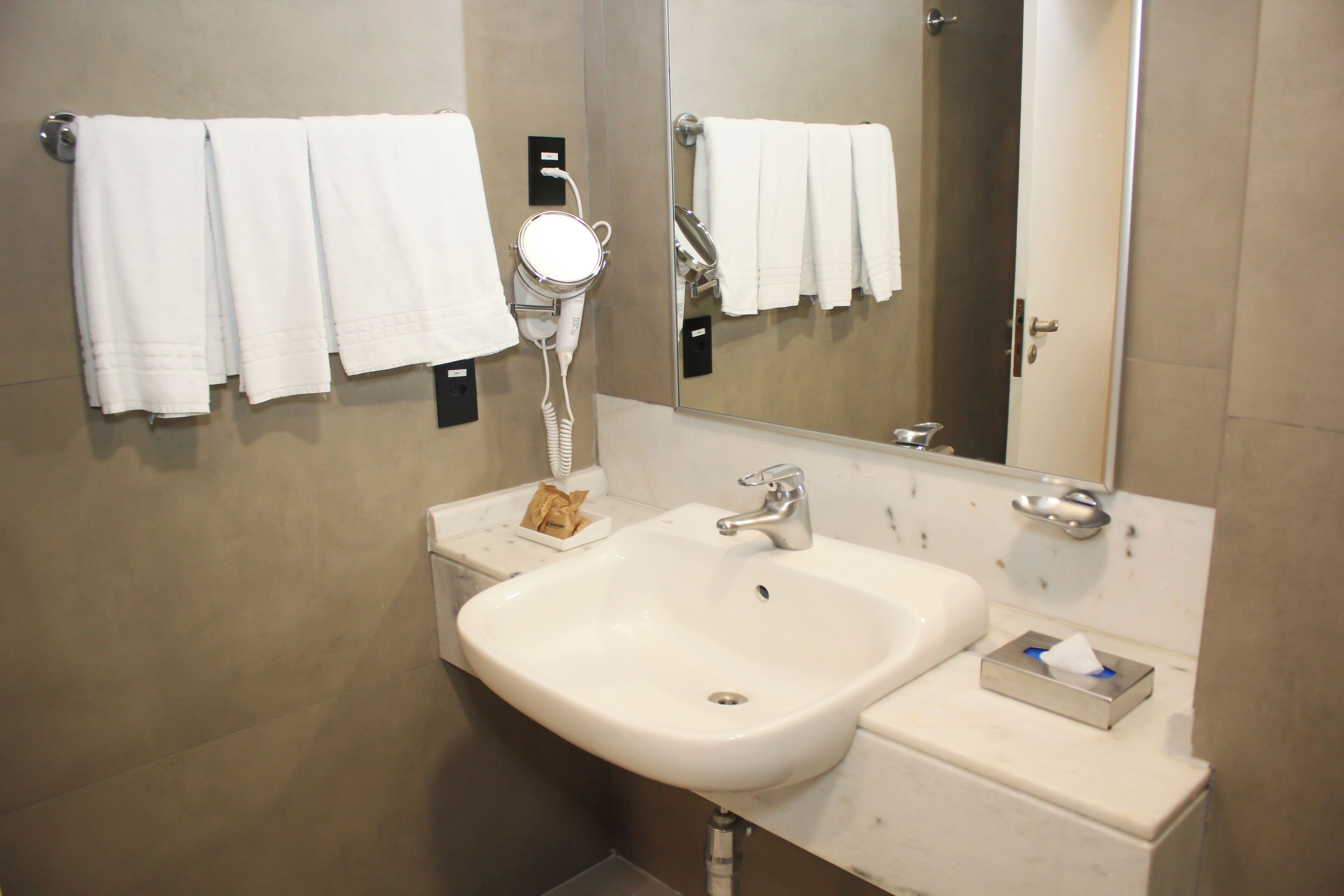 Une salle de bain avec un lavabo blanc, un miroir et plusieurs serviettes blanches suspendues à un porte-serviettes.