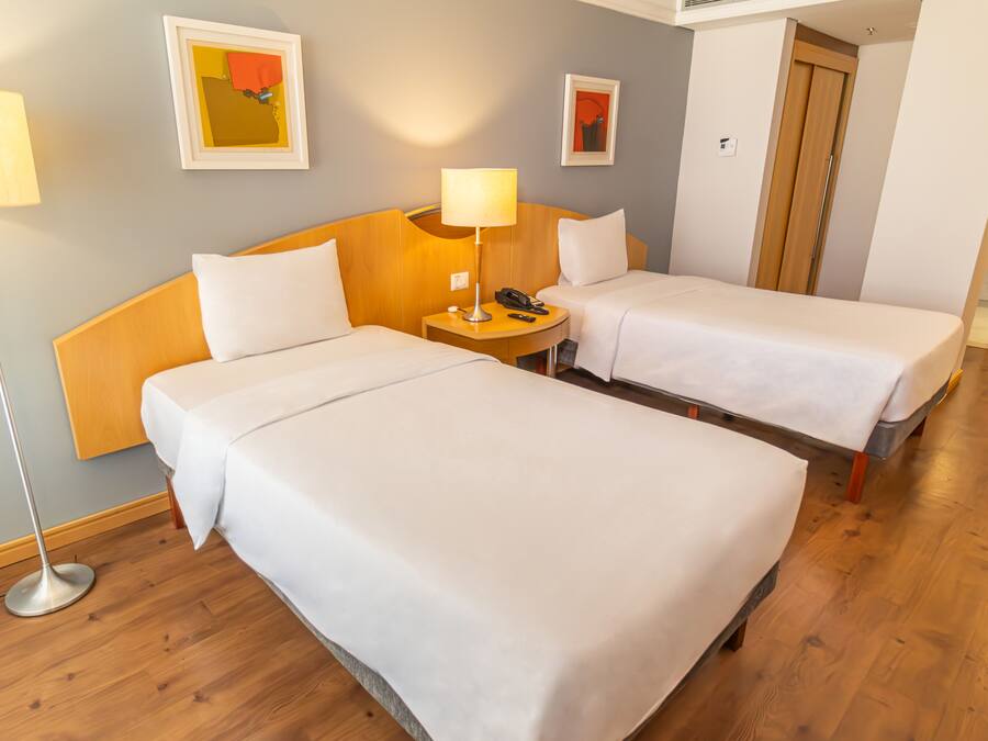 A hotel room with two beds, a bedside table with a lamp, and artwork on the walls.