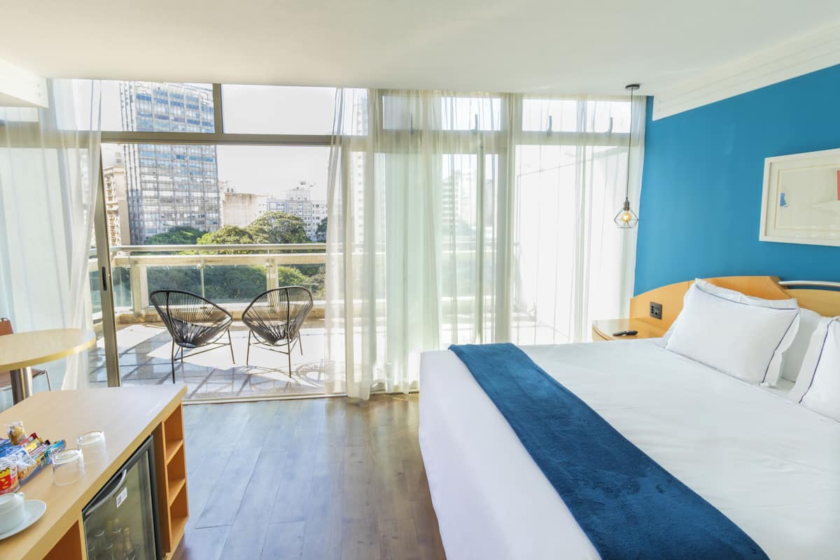 Hotellihuone, jossa on suuri sänky, työpöytä tuolilla sekä parveke, jolta on näkymä kaupunkiin.