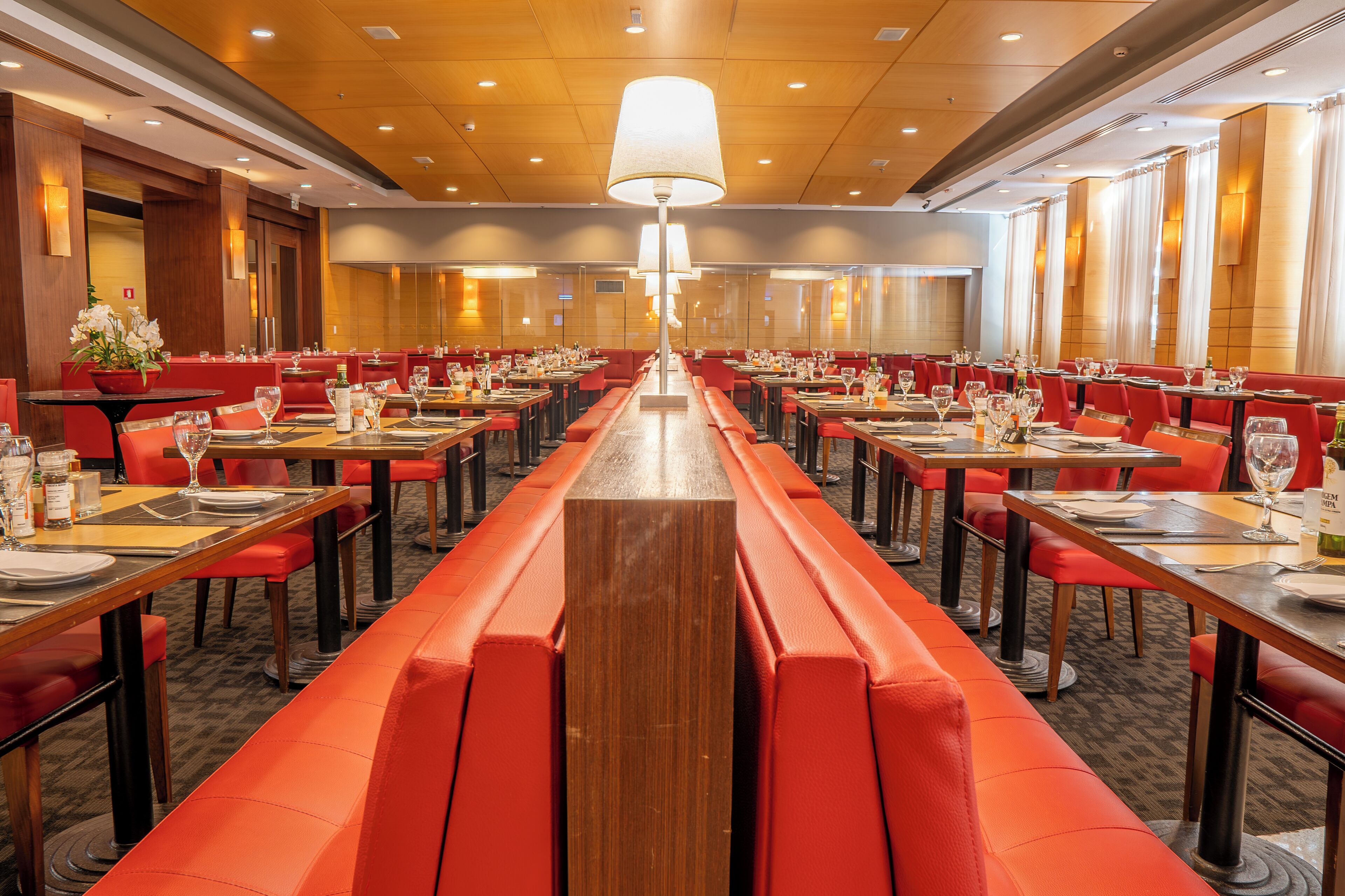 Ein geräumiges Restaurant mit roten Sitzbänken und Tischen, an jedem Tisch Weingläser und Besteck.