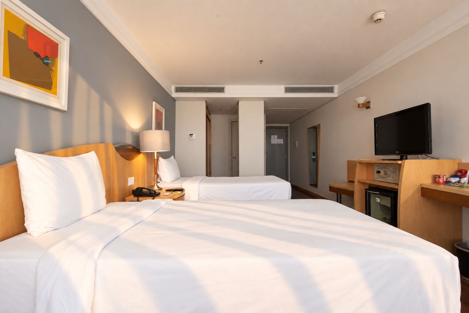 A hotel room with two beds, a desk with a television, and a minibar.