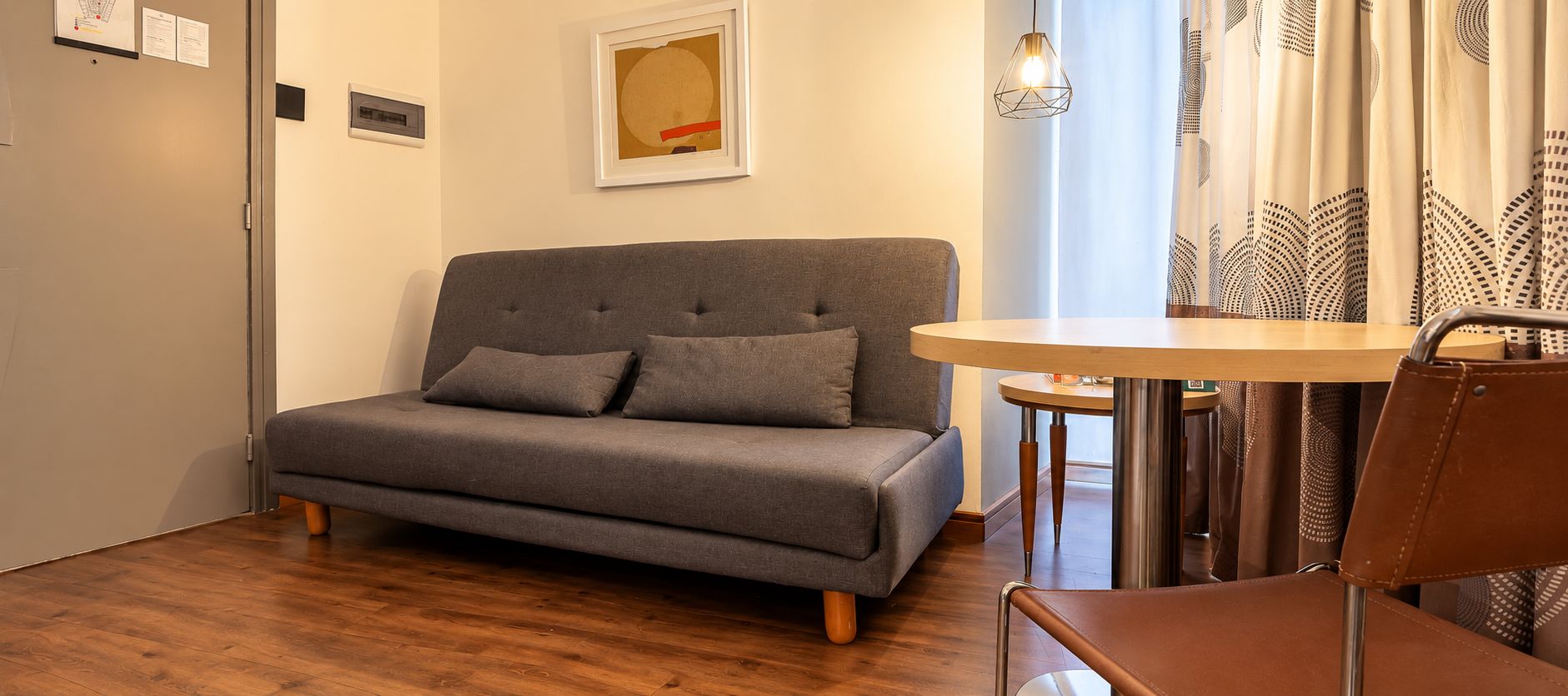 A modern living room with a grey sofa, a small round table, and a brown leather chair.
