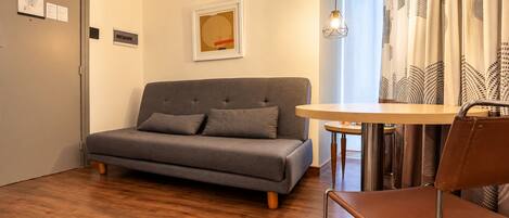 A modern living room with a grey sofa, a small round table, and a brown leather chair.