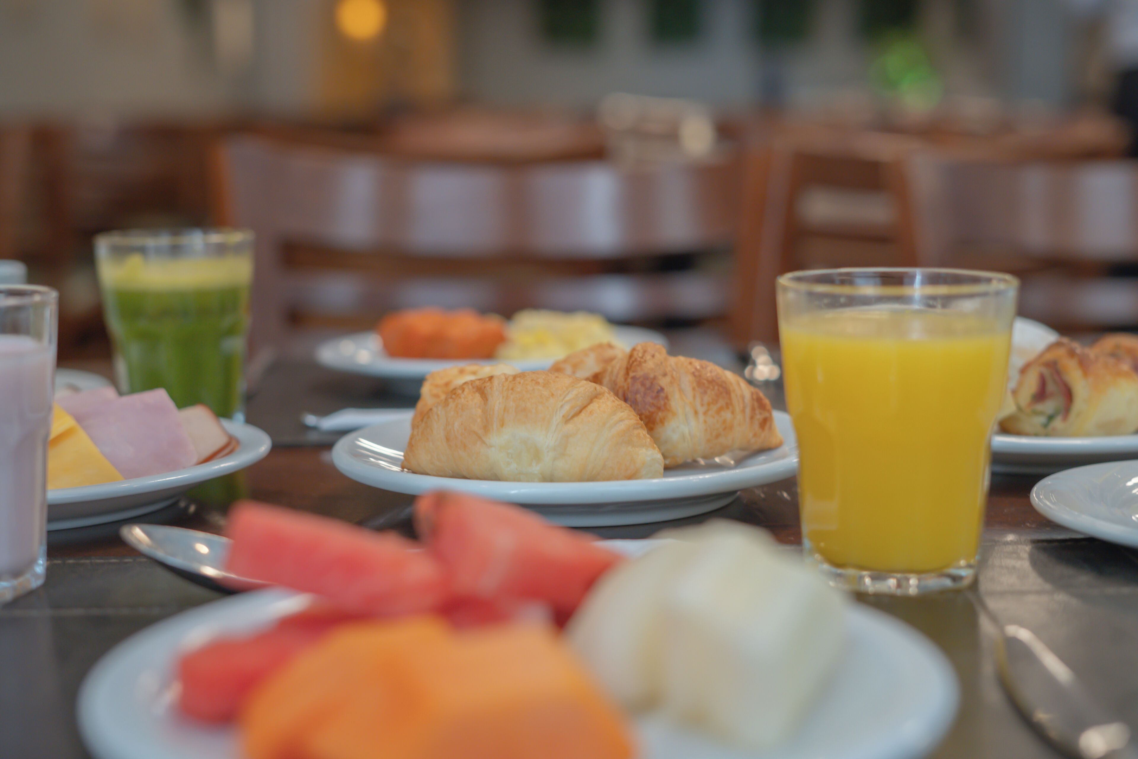 A breakfast setting with plates of croissants, fruits, and juices.