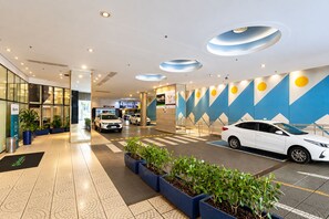 Eine moderne Hotelhalle mit Parkplatz, Blumentöpfen und einem auffälligen, geometrischen Wanddesign.