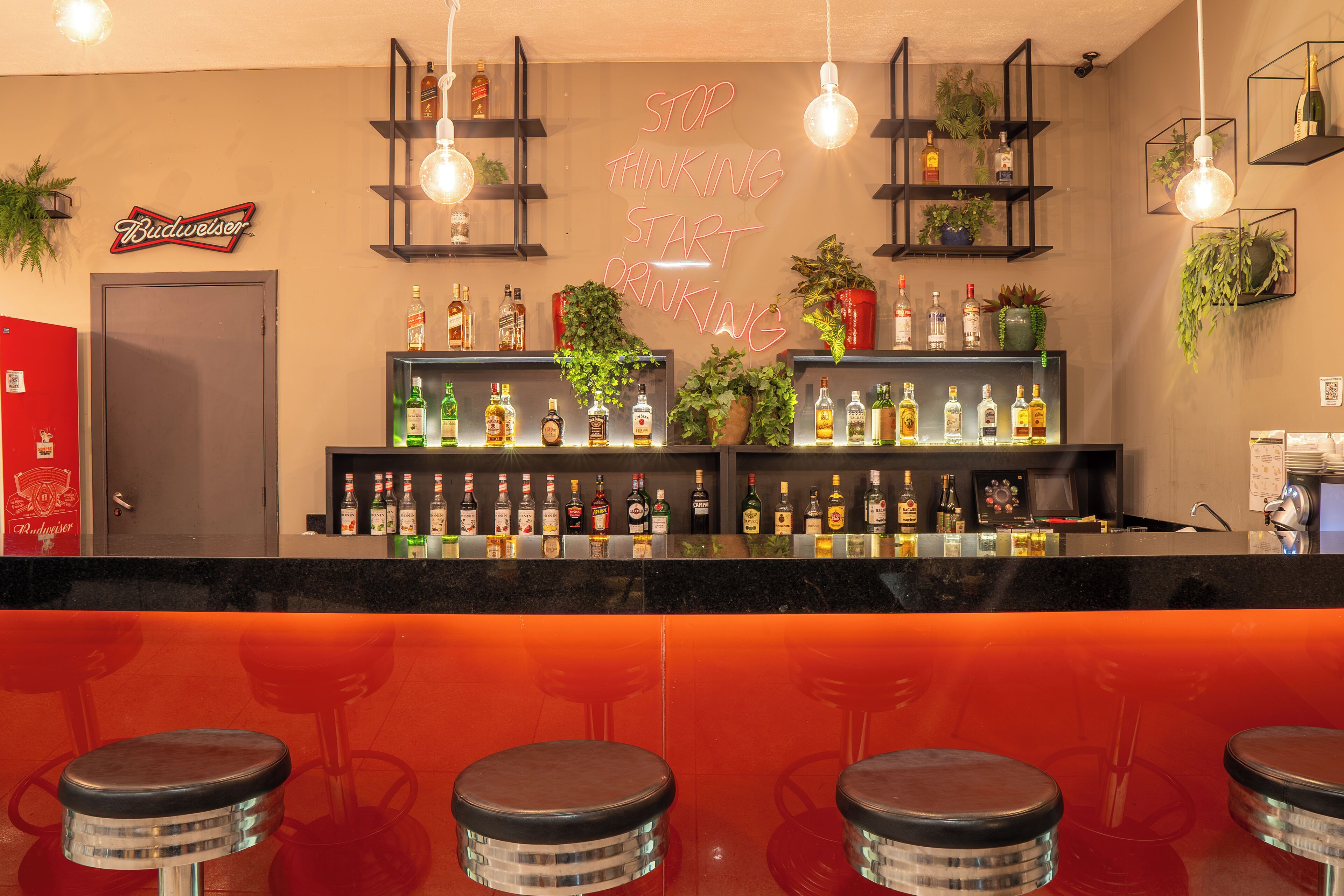 Zona de bar con un letrero de neón, estantes con botellas y taburetes.