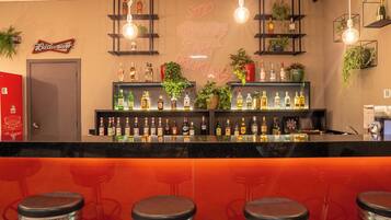 Zona de bar con un letrero de neón, estantes con botellas y taburetes.