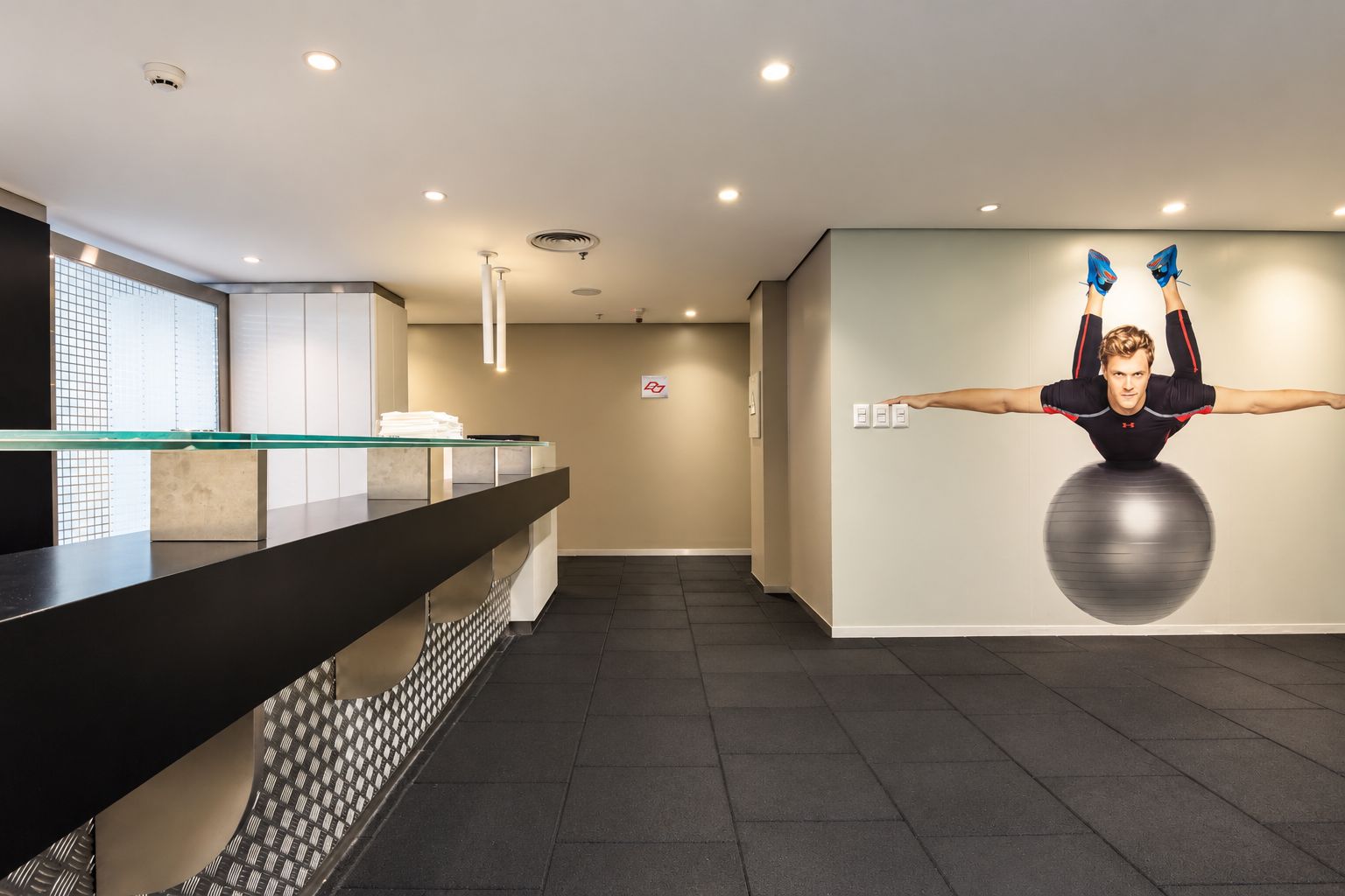 Un espace d’accueil doté d’un comptoir en verre, d’un ballon d’exercice fixé au mur et d’un plafond équipé de luminaires encastrés.