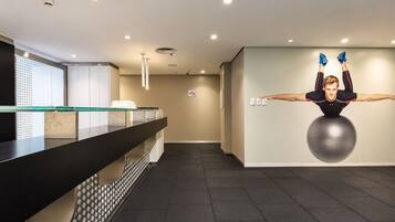 Een receptiegedeelte met een glazen balie, een wandgemonteerde fitnessbal en een plafond met inbouwverlichting.