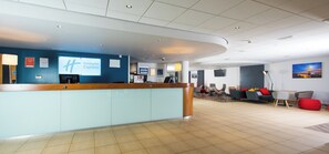 A hotel reception area with a counter, seating area, and a large screen displaying the hotel name. - Holiday Inn Express Newport by IHG (Newport)