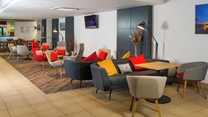 A modern lounge area with sofas, chairs, and a table, featuring a flat-screen TV mounted on the wall.