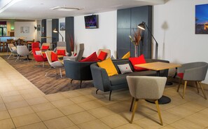 A modern lounge area with sofas, chairs, and a table, featuring a flat-screen TV mounted on the wall.