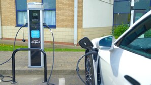 A charging station for electric vehicles, a white car parked nearby, and a building with a brick facade in the background. - Holiday Inn Express Newport by IHG (Newport)
