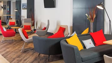 A modern lounge area with grey sofas, red and yellow cushions, and a wooden floor.
