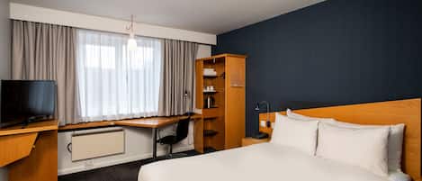 Une chambre d’hôtel avec un grand lit, un bureau avec un ordinateur, une armoire et un téléviseur.
