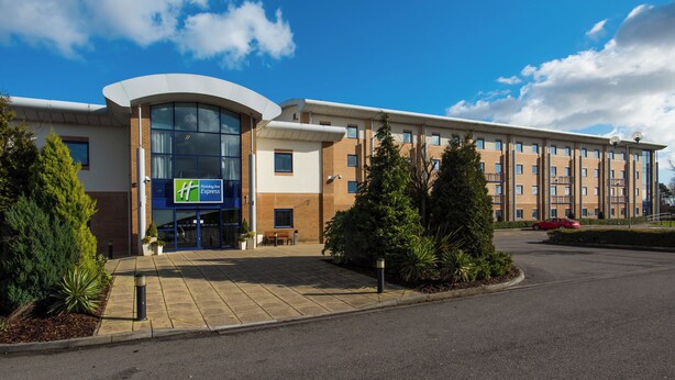 A Holiday Inn Express hotel with a curved glass entrance, brick facade, and a parking lot.