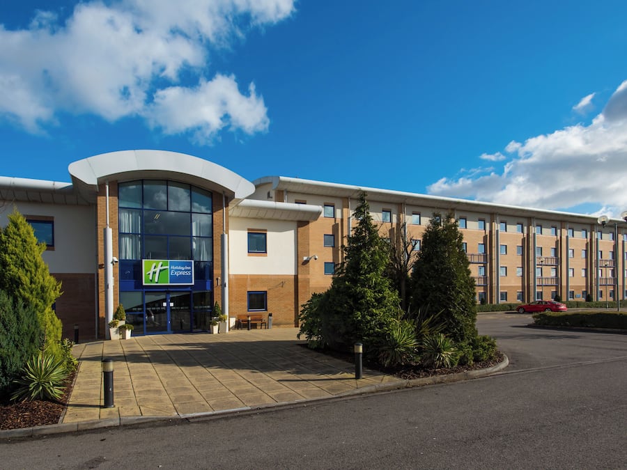 A Holiday Inn Express hotel with a curved glass entrance, brick facade, and a parking lot.