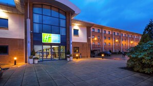 A Holiday Inn Express hotel with a large glass entrance, a curved facade, and a parking area with a few cars.