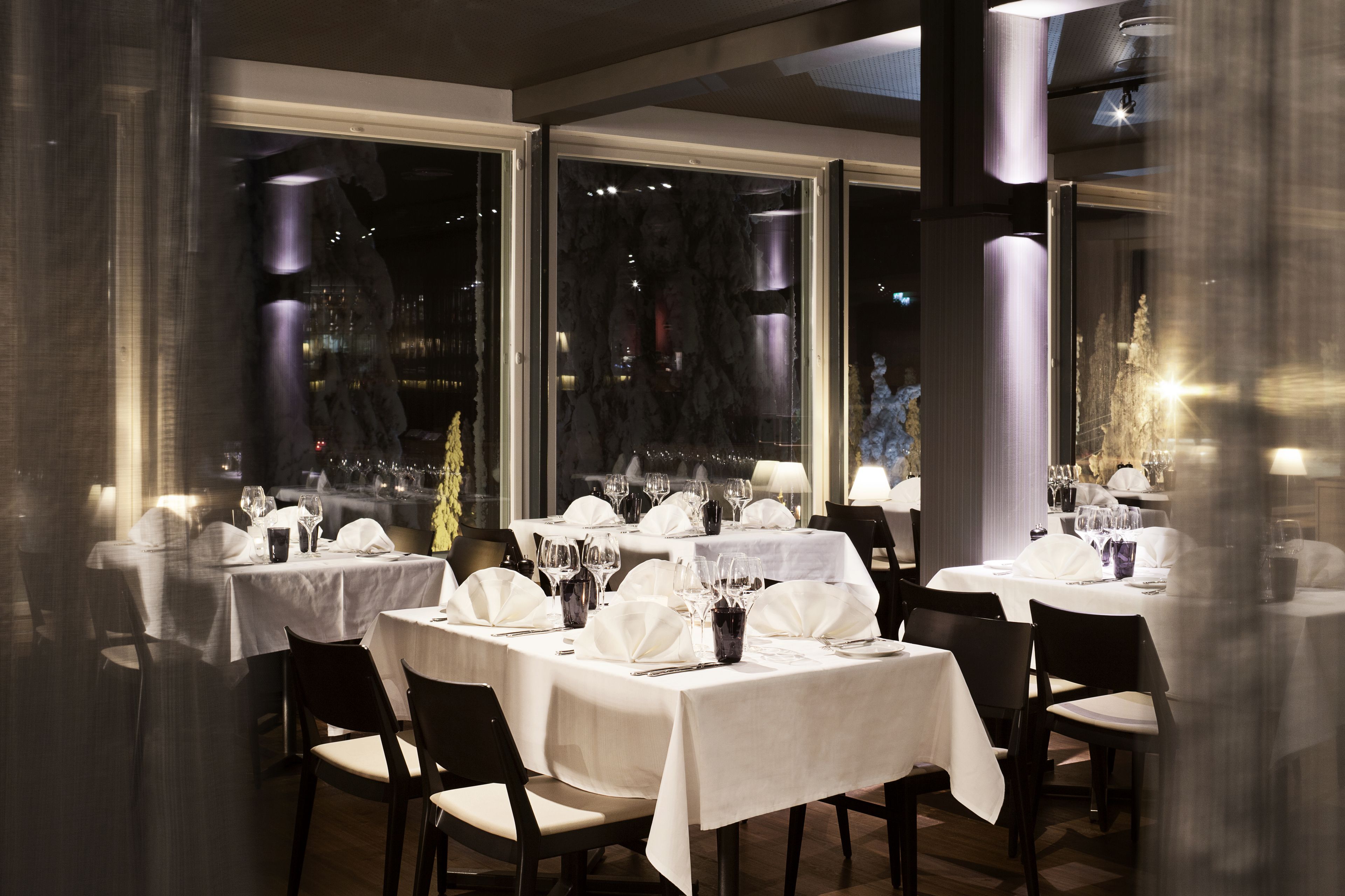 A restaurant with multiple tables set for dining, large windows, and a view of the cityscape.