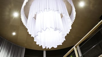 Un intérieur moderne avec un lustre circulaire blanc, un escalier doté de rampes en verre et un plafond haut.