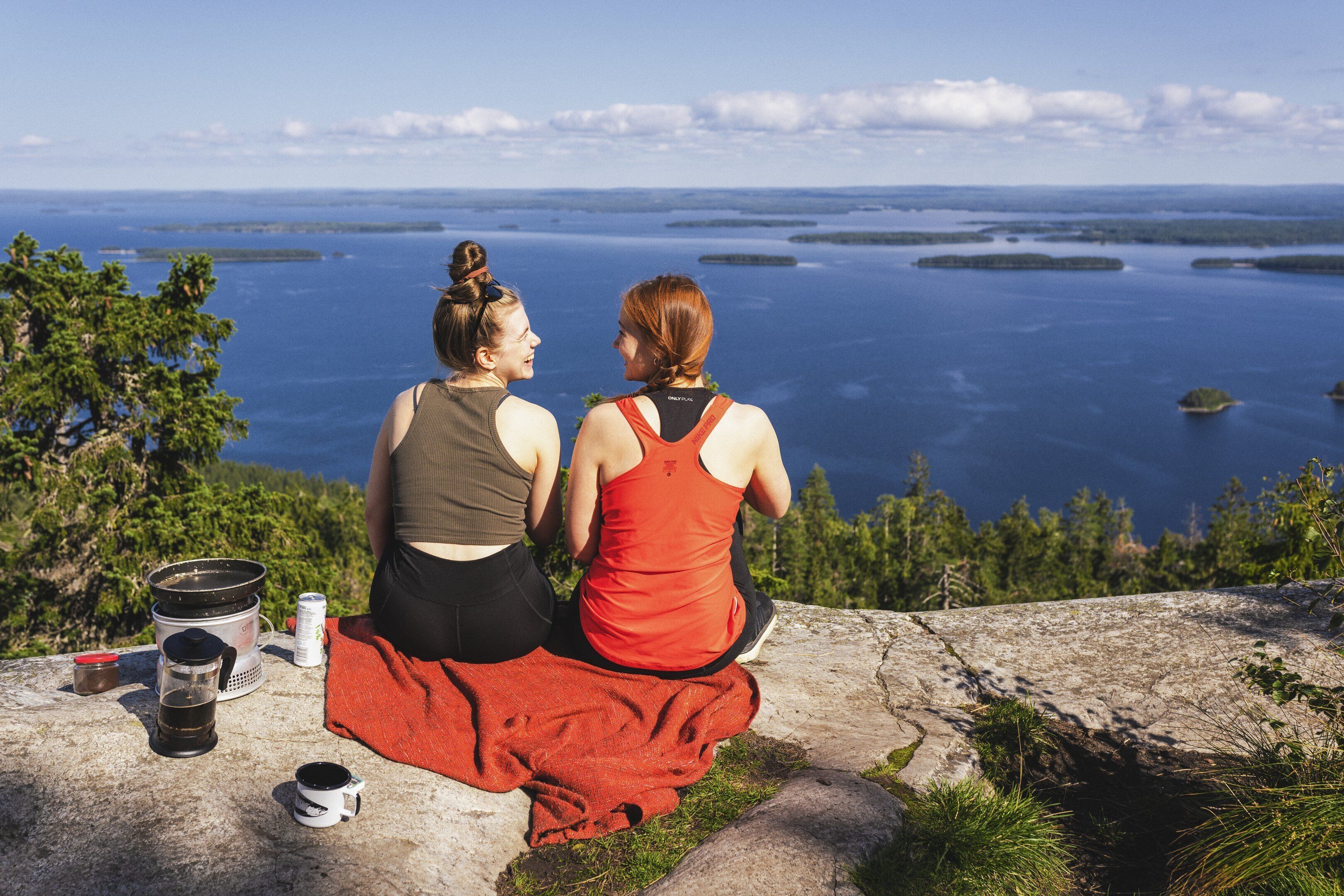 Two people sitting on a rock overlooking a body of water with islands in the distance.