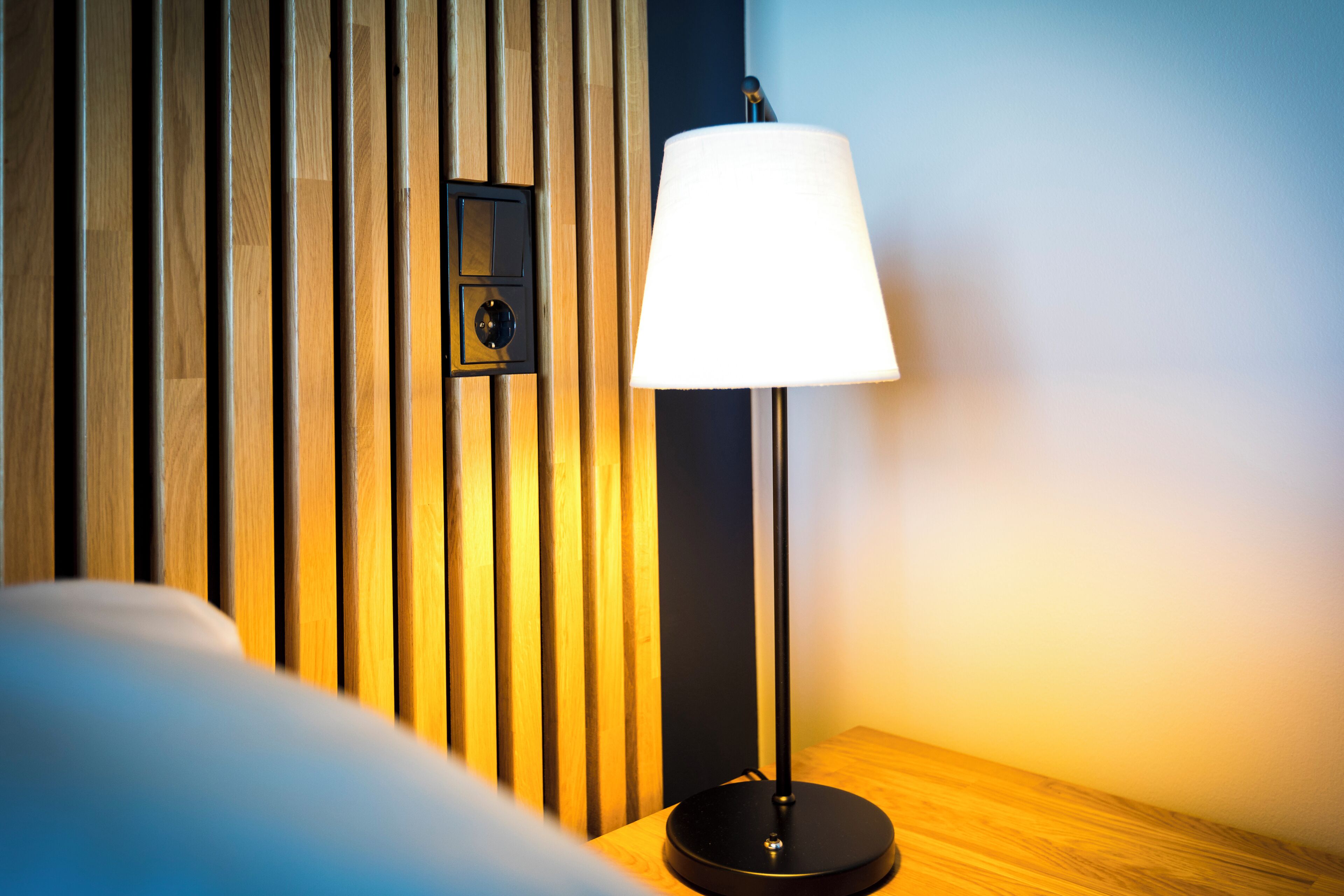 Une chambre moderne avec un mur lambrissé en bois, un lampadaire noir doté d’un abat-jour blanc et une table de chevet en bois.