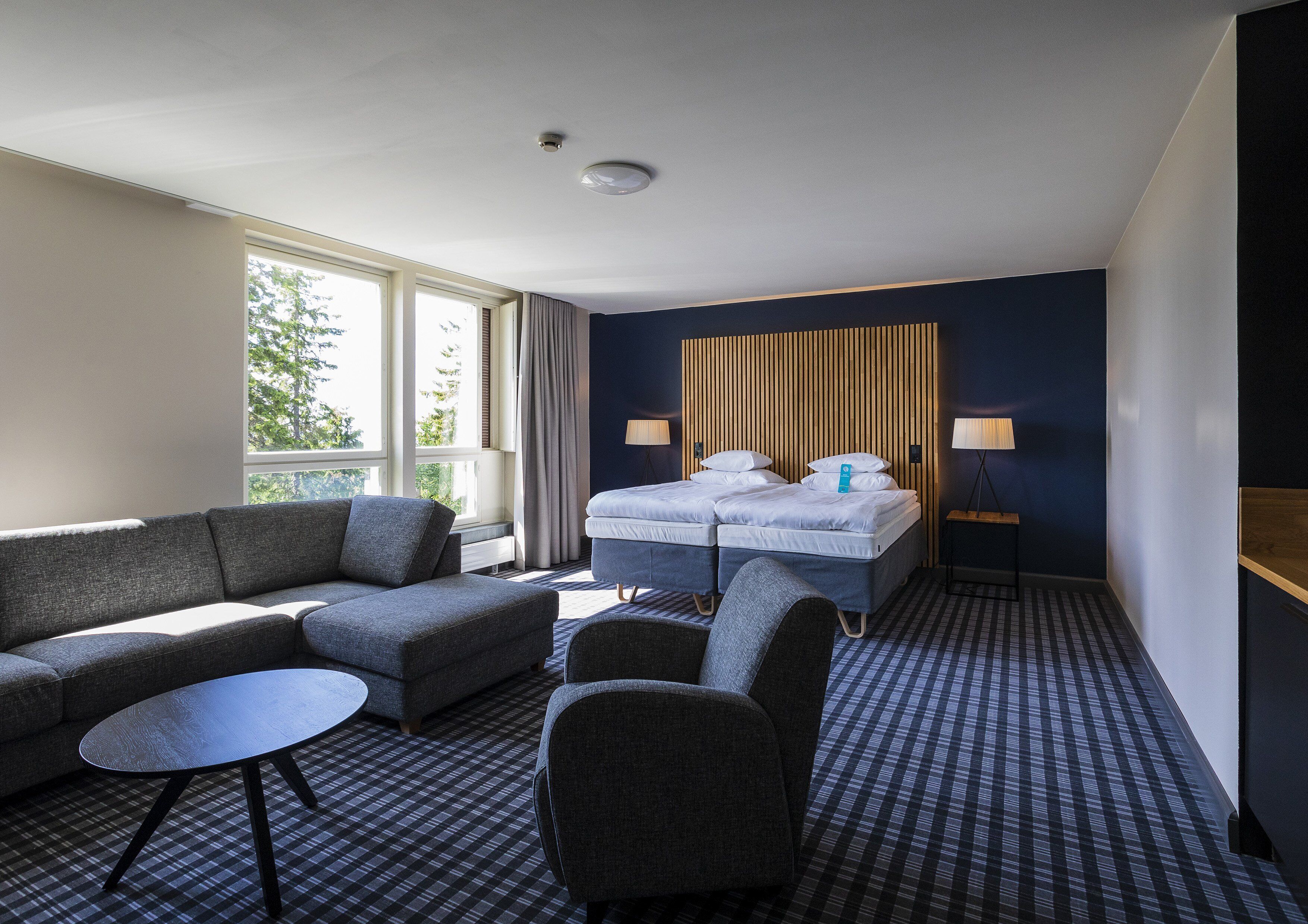 A hotel room with a large bed, a sofa, a chair, a small table, and a lamp.