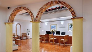 Un área de recepción con mostrador de entrada, sillas de madera y piso de baldosas.