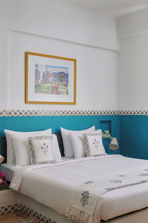 A neatly made bed with white linens and decorative pillows, a framed picture on the wall, and a blue accent wall. - The Gordon House Hotel (Mumbai)
