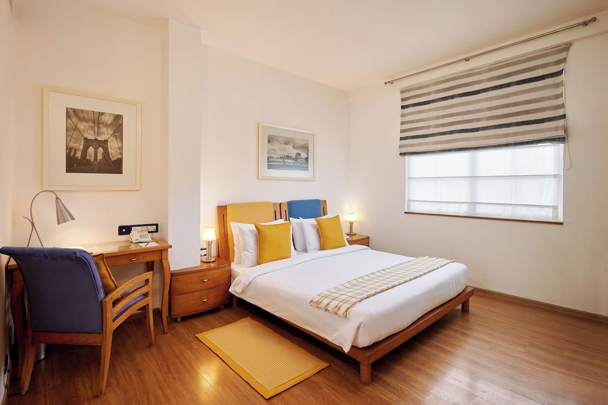 A bedroom with a wooden bed, a desk, a chair, and two bedside tables with lamps.