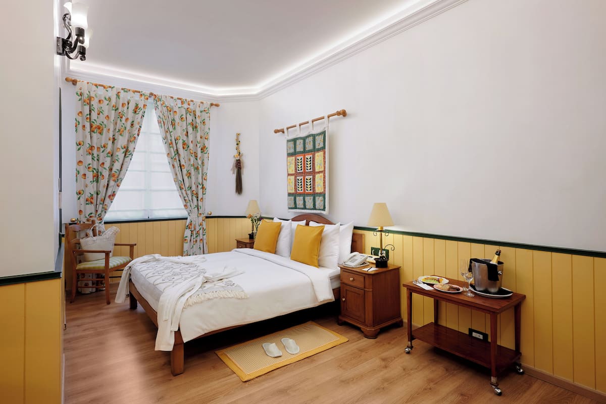 A neatly arranged bedroom with a bed, bedside tables, a nightstand, a small table with a bottle and glasses, and a chair.