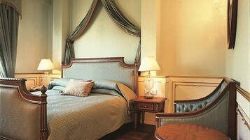A traditional bedroom with a four-poster bed, two bedside tables with lamps, a round wooden table, and a mirror on the wall.