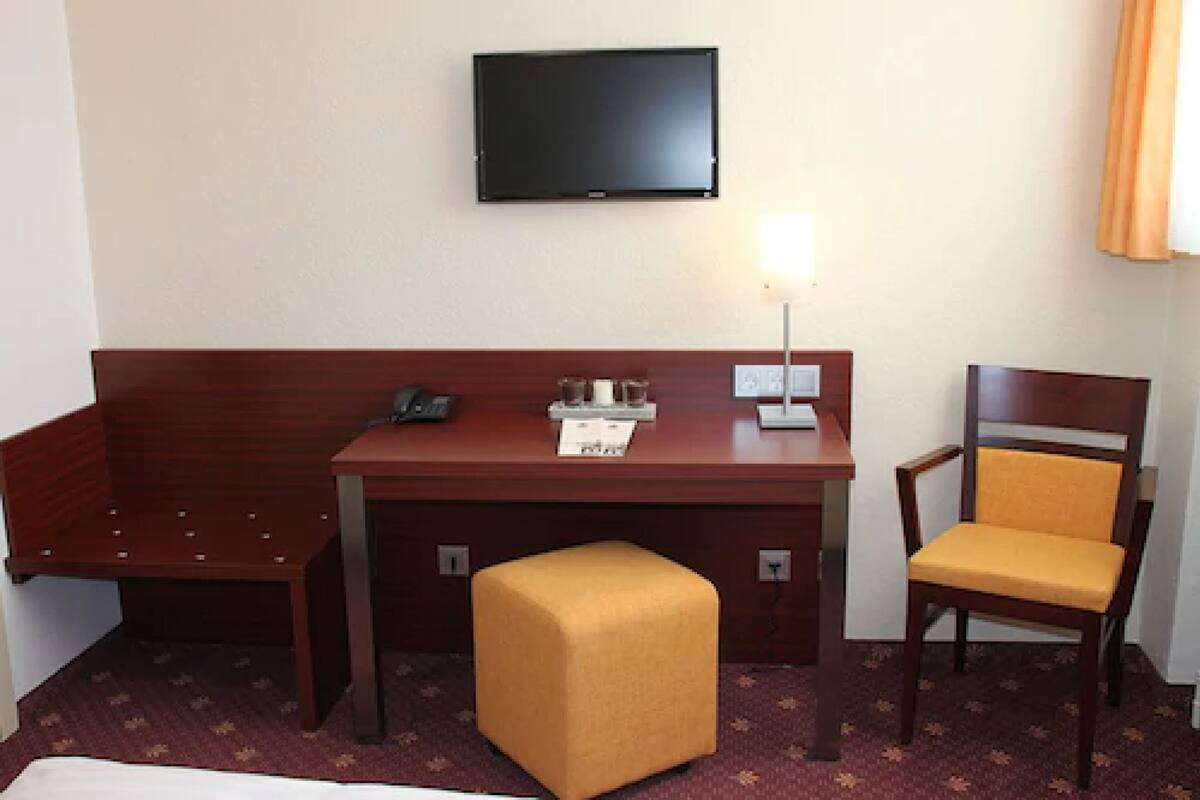 Habitación de hotel con un escritorio de madera, un televisor fijado a la pared, un taburete y una silla.