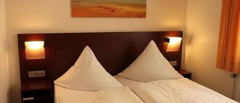 A double bed with white linens, two bedside tables with lamps, and a painting on the wall.