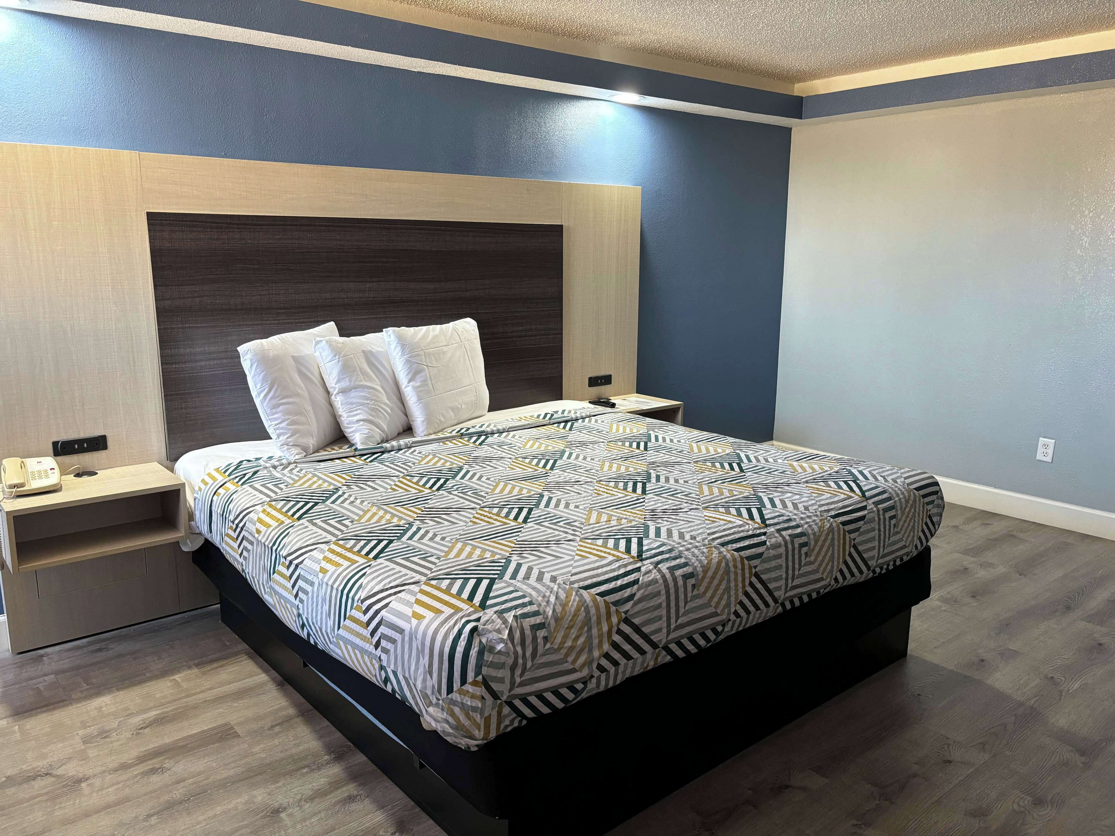 A modern bedroom with a large bed, a bedside table with a phone, and a nightstand.