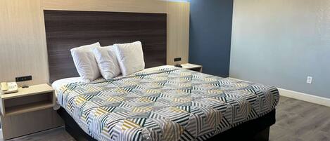 A modern bedroom with a large bed, a bedside table with a phone, and a nightstand.
