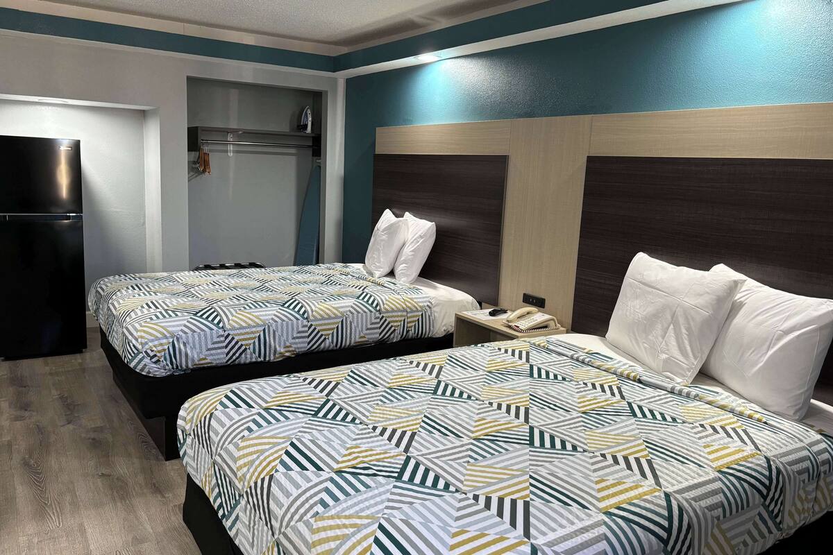 Ett hotellrum med två sängar, ett kylskåp, ett nattduksbord med en telefon och en väggmonterad värmare.