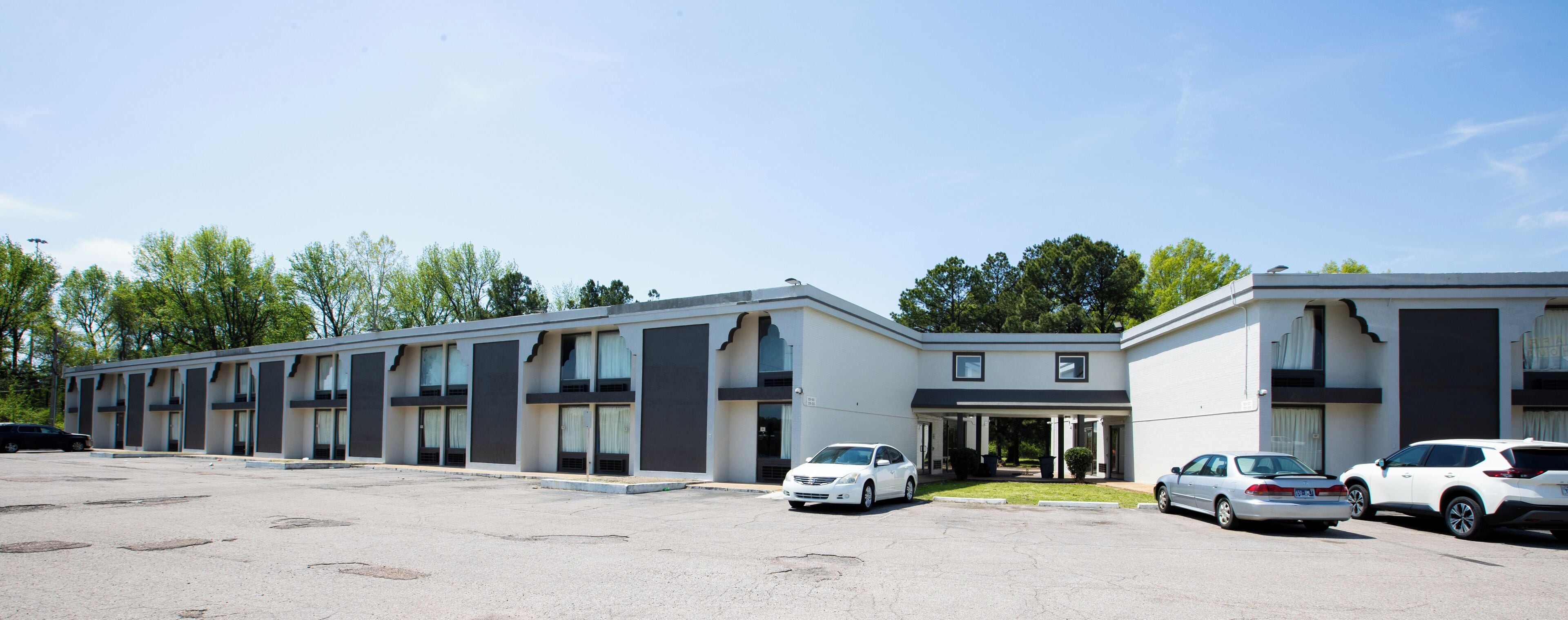 A motel with a row of rooms, a parking lot, and a small garden area.