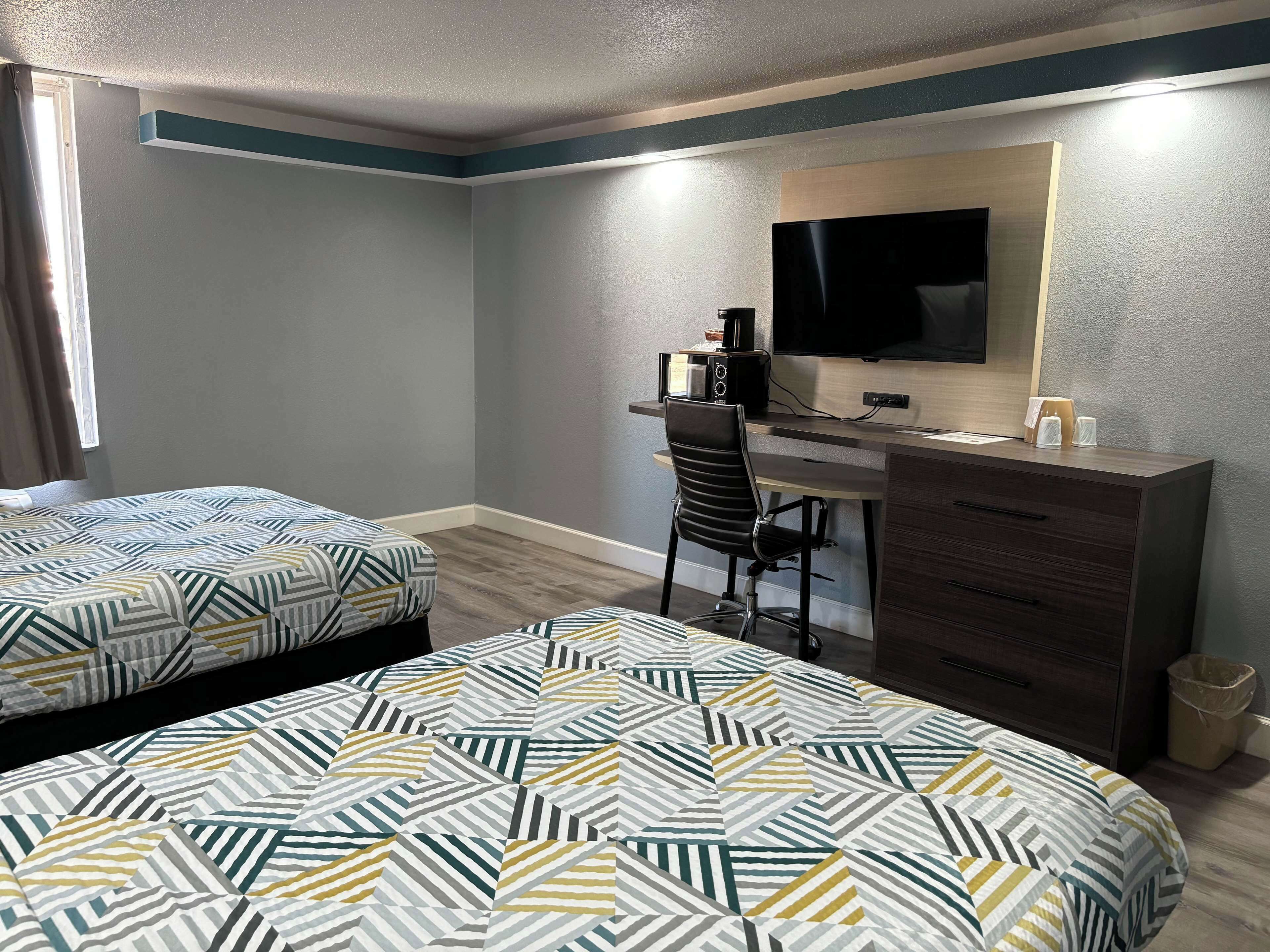 A hotel room with two beds, a desk, a chair, a TV, and a dresser.