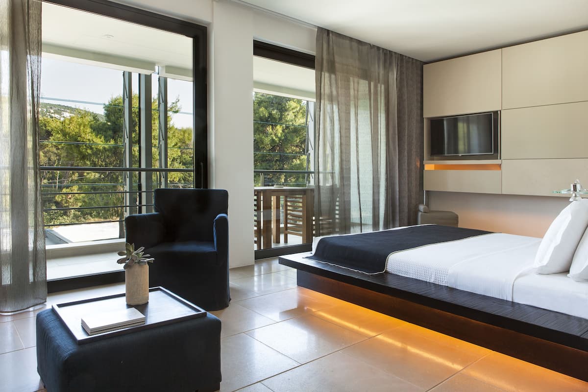 Quarto de hotel moderno com cama, TV, poltrona, mesa de centro e varanda com vista.
