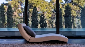 Un fauteuil moderne doté d’un coussin, placé devant de grandes fenêtres offrant une vue sur une forêt dense.