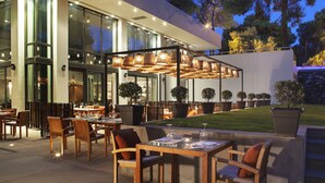 An outdoor dining area with tables and chairs, a pergola with hanging lights, and potted plants.