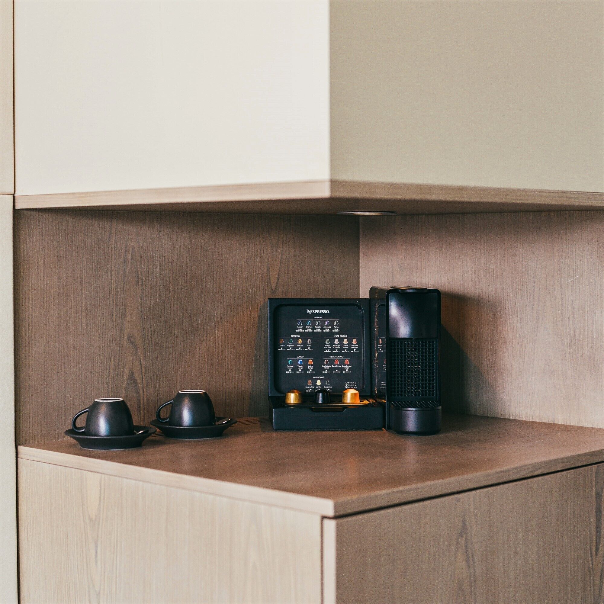 Una máquina de café Nespresso sobre una encimera de madera con dos tazas negras.