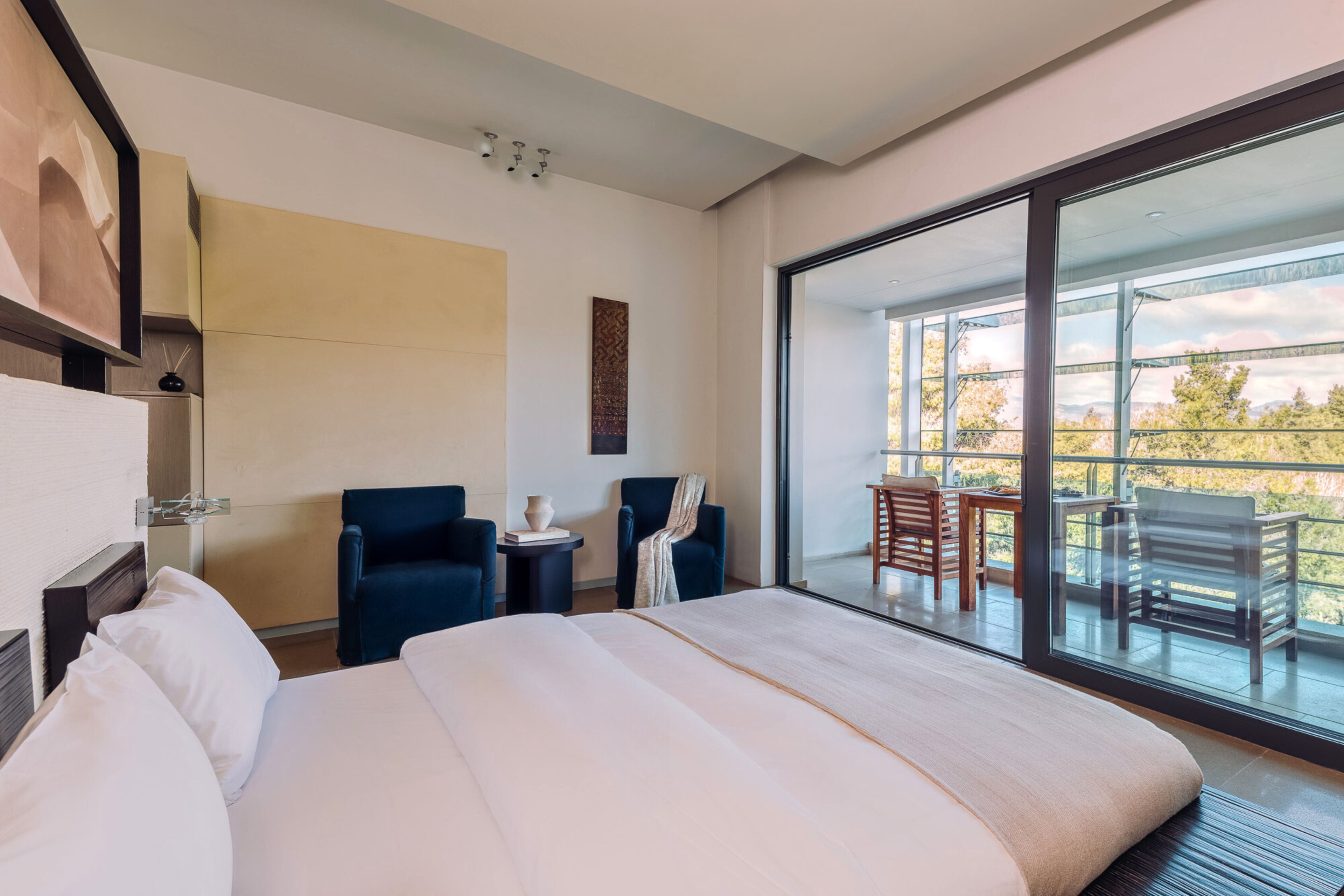 Une chambre d’hôtel moderne dotée d’un grand lit, de deux fauteuils, d’une petite table et d’un balcon avec un espace salon extérieur.