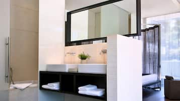 A modern bathroom with a large mirror, a white sink, and a built-in shelf with folded towels.