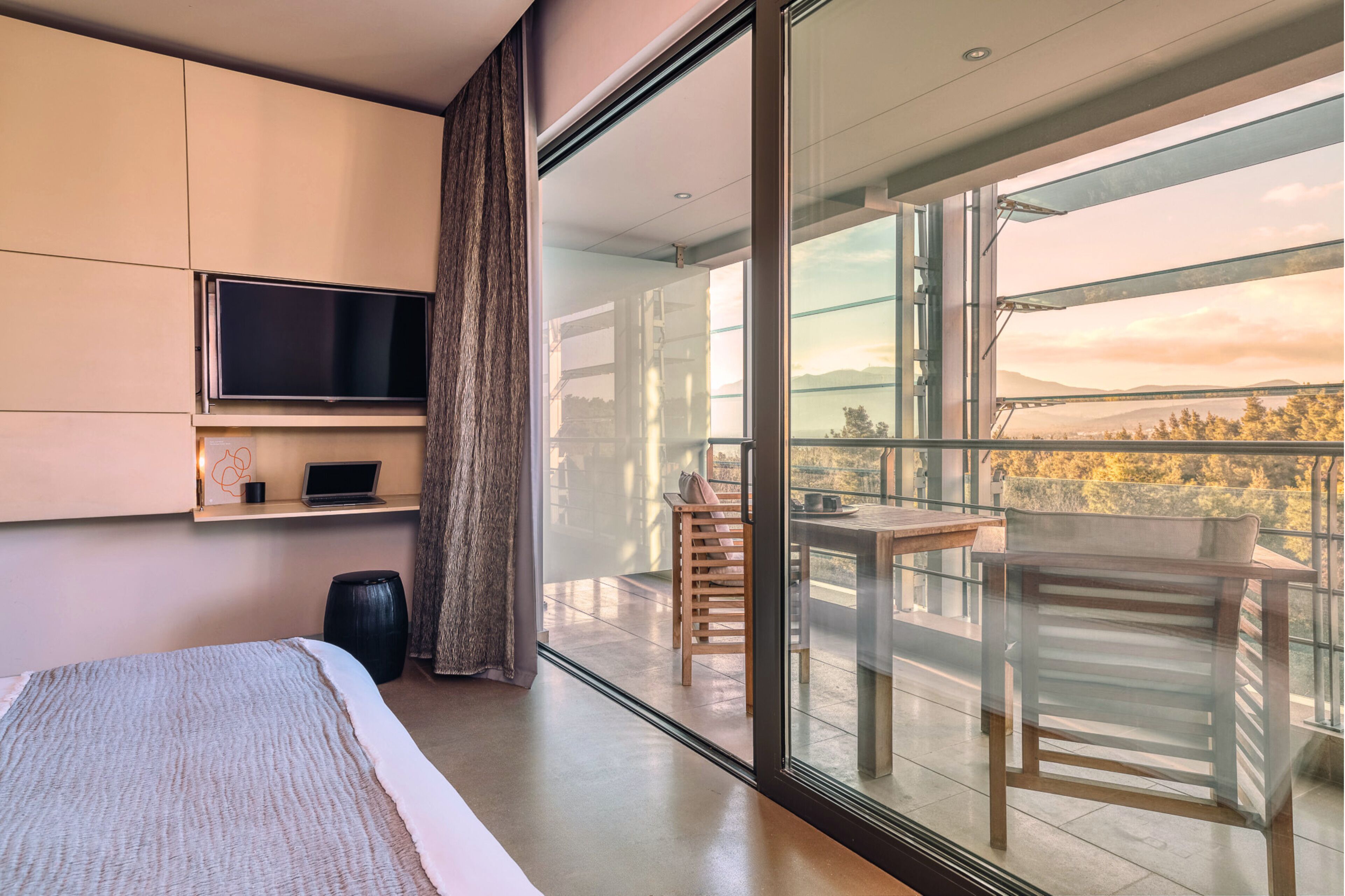 Un dormitorio moderno con una cama grande, un televisor en la pared y un balcón con mesa y sillas.