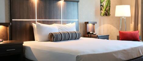 A hotel room with a large bed, two bedside tables, a nightstand, a lamp, and a wall-mounted artwork.