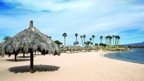 A beach with thatched umbrellas and palm trees. - Avi Resort & Casino (Laughlin)