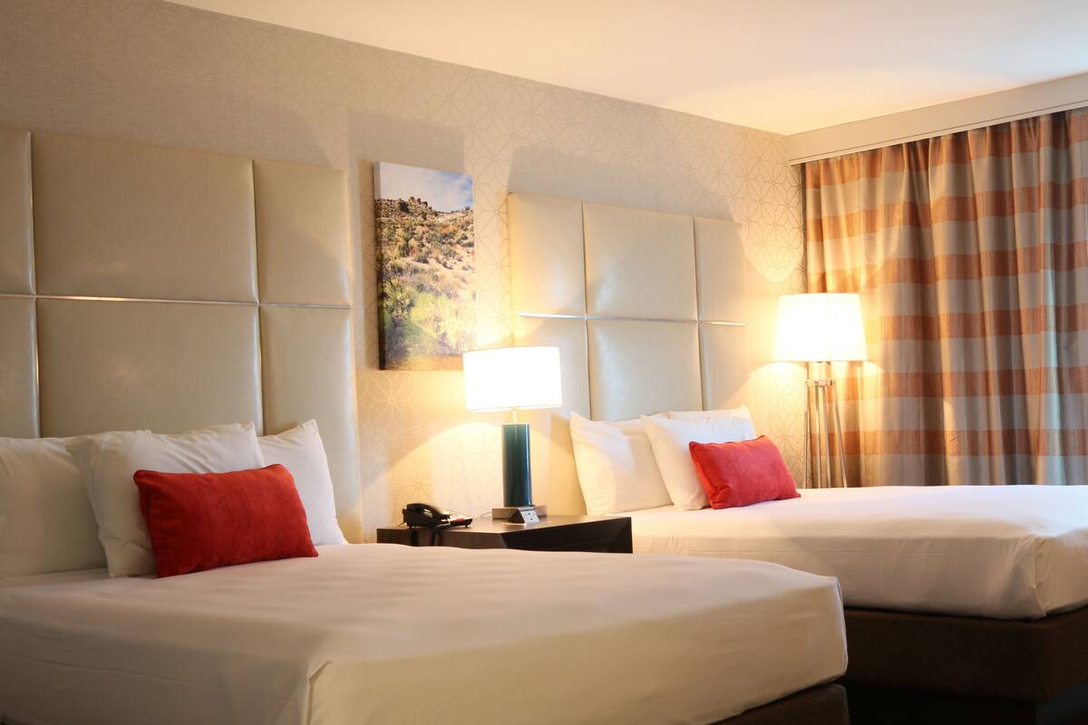 Ein Hotelzimmer mit zwei Betten, einem Kopfteil, einem Gemälde, einer Lampe und einem Vorhang.